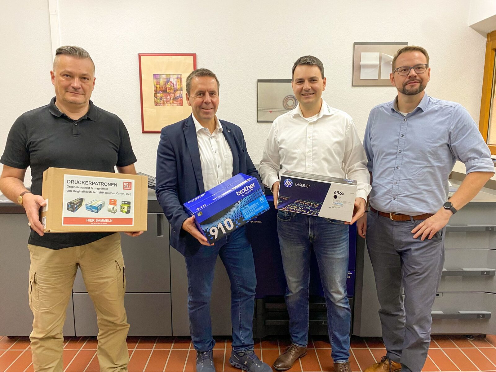 Vier Männer halten im Landratsamt Roth eine Sammelbox und originalverpackte Tonerkartuschen von Brother und HP in die Kamera